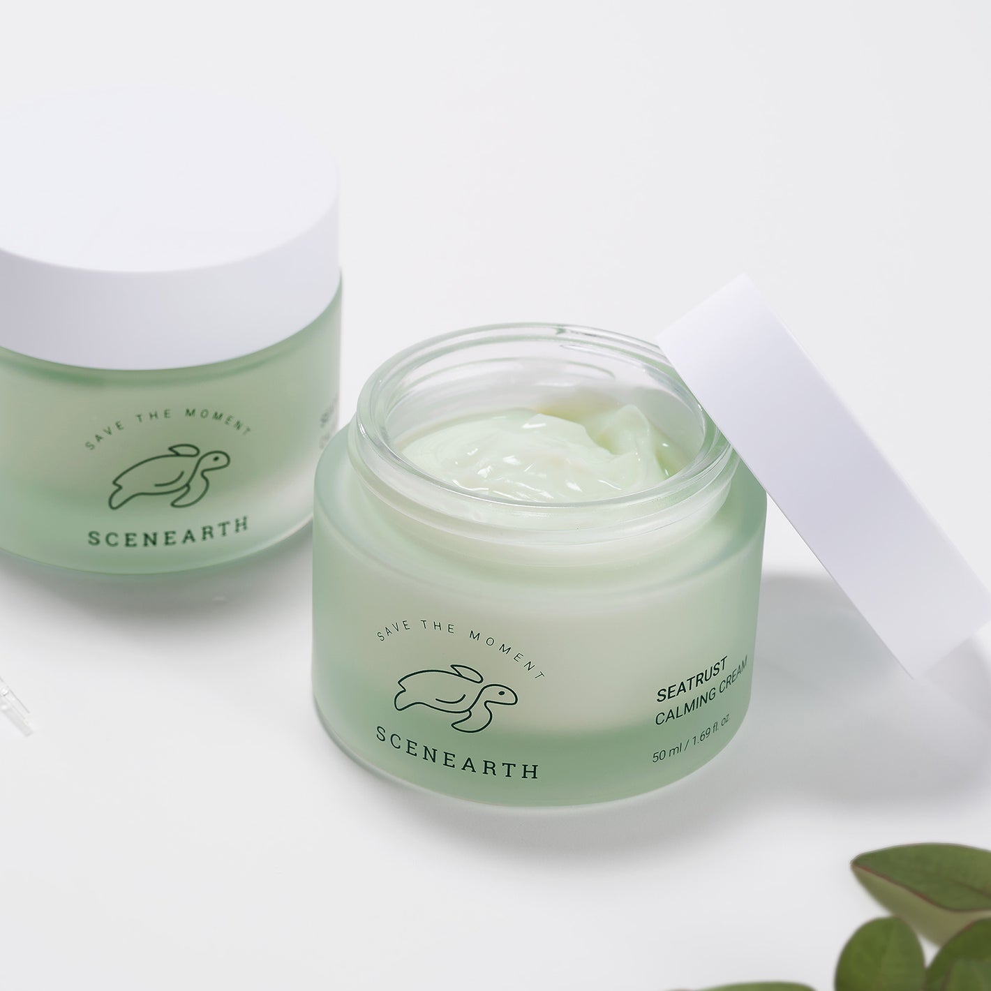 Two Scenearth Seatrust Calming Cream products next to some leafs in the lower right corner and in front of a white background
